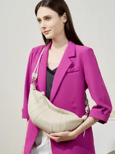 Beige leather croissant bag with stitched segments worn by a model in a purple suit
