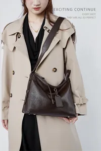 Detail of vintage brown leather tote bag with wide strap on beige trench coat