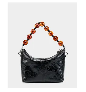 Détail du sac bandoulière en cuir ciré noir avec poignée en perles ambrées et métal