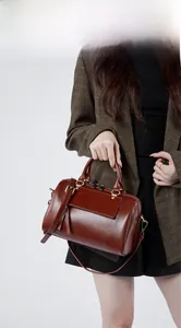 Brown leather Boston bag shown by model wearing a brown checkered blazer and black pants
