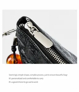 Détail du sac en cuir noir façon croco avec fermeture éclair argentée et perle d'ambre
