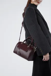 Detailed side view of a burgundy leather Boston bag with tassel on a model