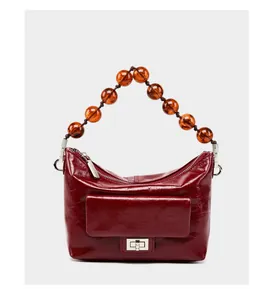 Détail d'un sac à main bordeaux en cuir ciré avec poignée en perles et fermoir rotatif