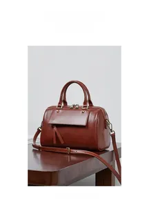 Close-up of vintage brown leather Boston bag with tassel detail on dark wood surface