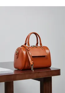 Detail view of a vintage brown leather boston bag with bronze hardware on a wooden table