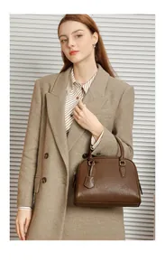 Dettaglio della borsa Boston in pelle marrone con fibbie dorate indossata da una modella
