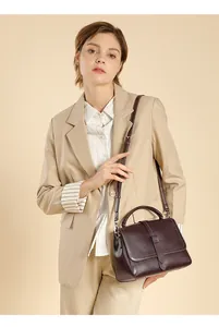 Detail of burgundy leather shoulder bag with buckle strap on a light blazer suit