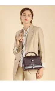 Detail of burgundy leather handbag with a textured woven shoulder strap on model