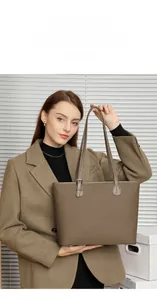 Close-up of a large clay-colored leather tote bag held by a model for size perspective