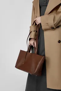 Dettaglio della borsa tote in pelle marrone con trama fine e piedini dorati alla base