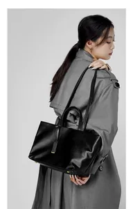Dettaglio della borsa tote in pelle nera indossata con un elegante trench grigio
