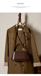 Detail view of a dark brown leather crossbody bag with dual zippers and metal bottom studs