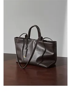 Dettaglio della borsa tote in pelle marrone scuro con trama fine e finiture oro
