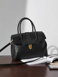 Dettaglio borsa ventiquattrore in pelle nera con chiusura dorata su tavolo in legno