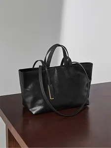 Dettaglio borsa tote minimalista in pelle nera con doppi manici e targhetta in metallo