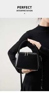 Detail of a black leather square handbag with top handle and adjustable shoulder strap