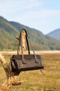 Deep brown vintage leather tote bag hanging on a branch in a natural autumn landscape