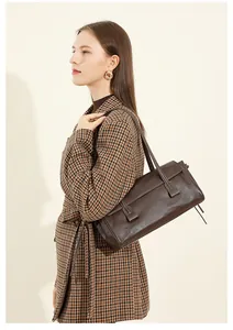 Close-up of vintage dark brown leather baguette bag worn over a plaid wool coat