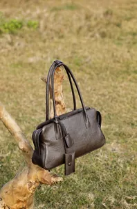 Detalle macro del bolso tote de cuero granulado marrón oscuro colgado de una rama