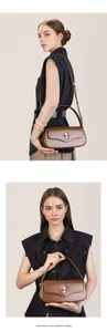 Detail of dark brown leather baguette bag with golden cross-shaped metal lock and slim strap