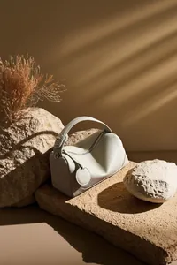 Dettaglio della pelle beige a grana e degli elementi metallici della borsa Boston