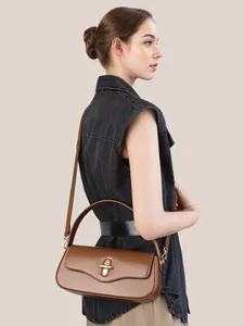 Caramel brown leather baguette bag with gold metal clasp on model over casual denim vest