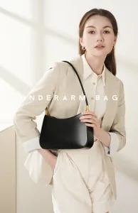 Close-up of minimalist black leather underarm bag with gold hardware worn by model