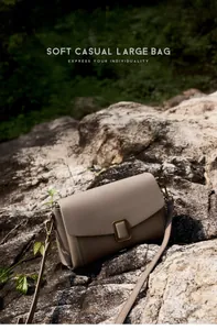 Detail of grey leather crossbody bag with vintage metal buckle on a rustic rock background