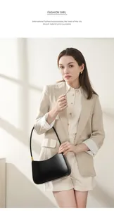 Minimalist black leather crescent shoulder bag with gold hardware on a model with a suit