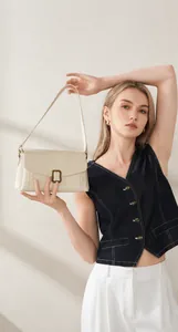 Gros plan d'un sac à bandoulière en cuir blanc crème avec fermoir doré sur modèle