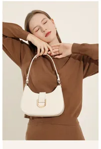 Detail einer beigen Hobo-Tasche aus Leder mit goldener Schnalle an einem braunen Pullover