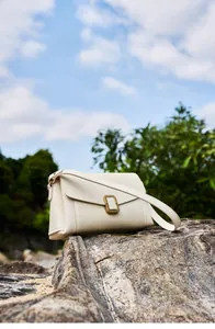 Creamy leather shoulder bag with vintage gold clasp on natural rock outdoor background