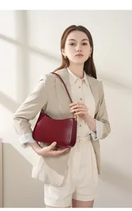 Minimalist burgundy leather shoulder bag with gold hardware detail on a model