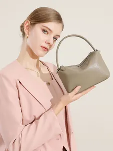 Borsa a mano minimalista in pelle talpa con manico curvo in un ambiente di moda elegante