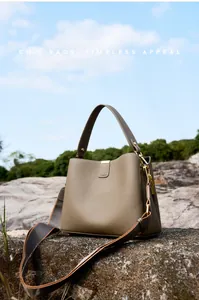 Borsa a secchiello in pelle martellata verde oliva con ampia tracolla su sfondo di roccia