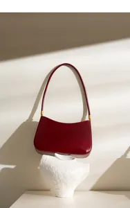 Close-up of a burgundy leather shoulder bag with gold hardware against a minimalist shadow