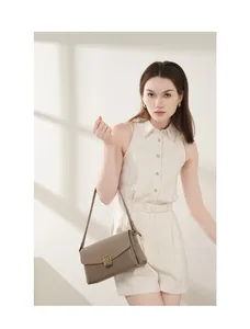Detail of tan leather shoulder bag with gold square buckle worn by a model in soft light