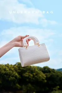 Détail du sac à main beige en cuir verni à motif crocodile et anneaux dorés