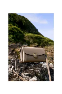 Taupe vegetable tanned leather shoulder bag with vintage gold buckle on natural rock
