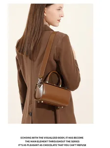 Close-up of brown leather box bag featuring wide strap and silver protective feet