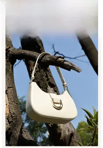Detailansicht der cremefarbenen Ledertasche mit goldenen U-Metallteilen im Freien