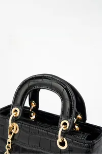 Détail d'un sac à main noir en cuir verni gaufré crocodile et finitions dorées