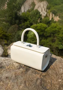 Side angle of beige leather box bag with metal twist lock and circular handle on stone