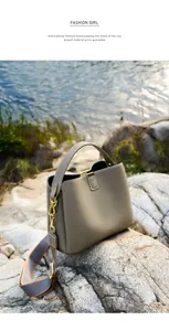 Dettaglio borsa a secchiello in pelle grigia con tracolla larga su rocce in riva al lago