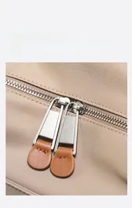 Macro shot of classic double metal zippers with brown leather pullers on khaki backpack