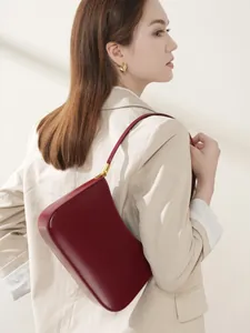 Deep red leather underarm bag with gold hardware worn by a model in a beige suit