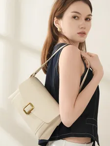 Creamy white vegetable tanned leather shoulder bag with a gold buckle worn by a model
