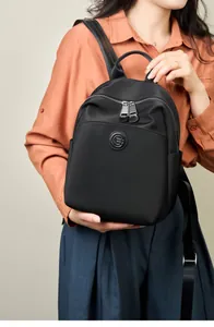 Model wearing a black nylon backpack with leather logo detail and dual zippers