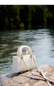 Détail de la texture croco blanc cassé avec anneaux dorés et chaîne sur le sac en cuir