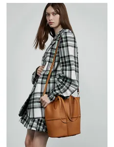 Brown leather tote bag with cross stitching detail worn by a model in a plaid blazer